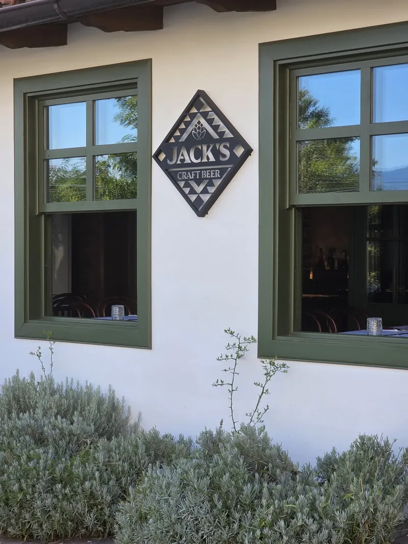 White facade with green window frames, a diamond-shaped Jack's Craft Beer sign and lavender below