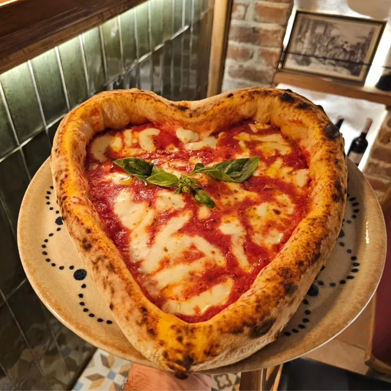 A heart-shaped pizza with tomato, mozzarella and basil held up over a table