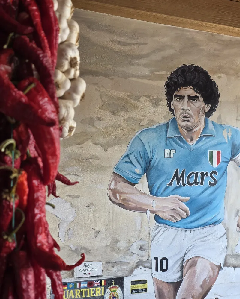 Wall mural of Diego Maradona in the light blue Napoli shirt, strings of red chilli peppers in the foreground