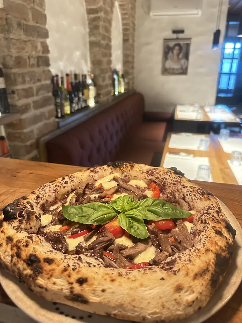 A Neapolitan pizza with beef, peppers and fresh basil on a wooden table, the dining room behind