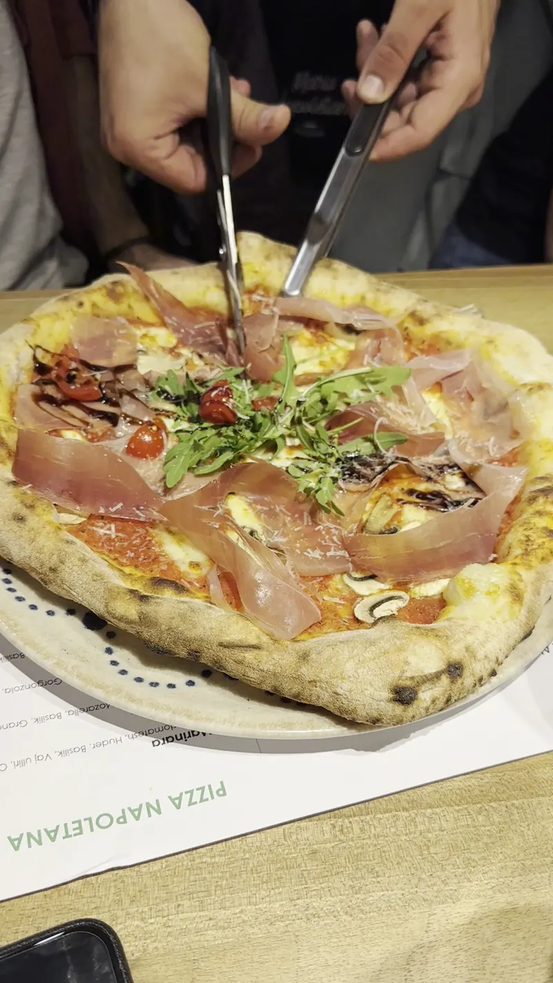 A pizza with prosciutto crudo and rocket being cut at the table